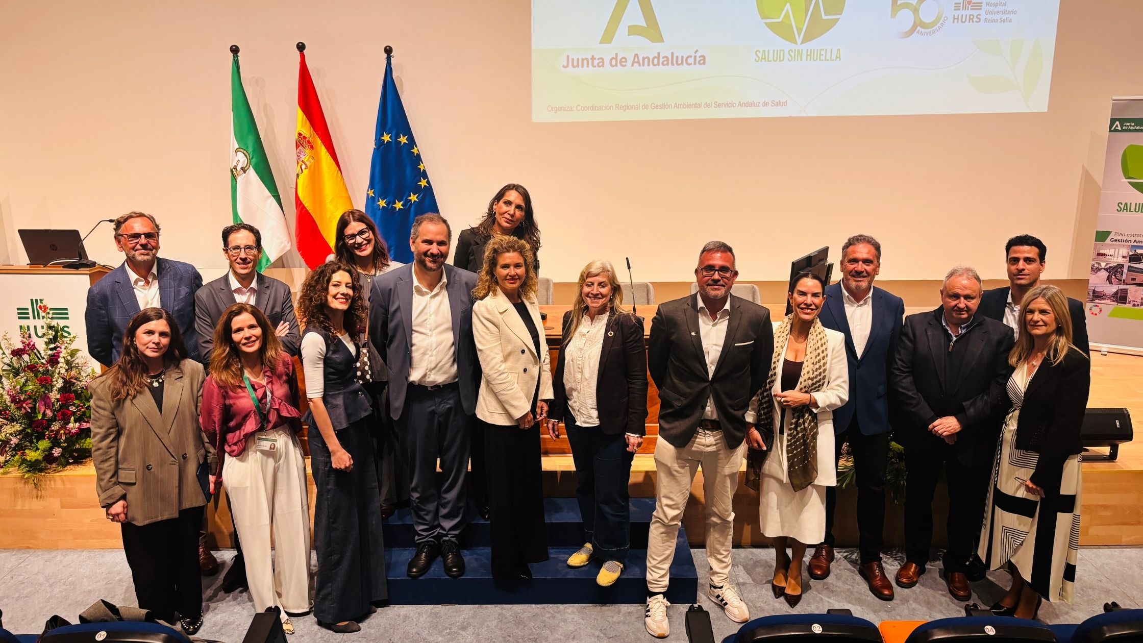 Personas posando delante de unas banderas y de un escenario en una jornada.